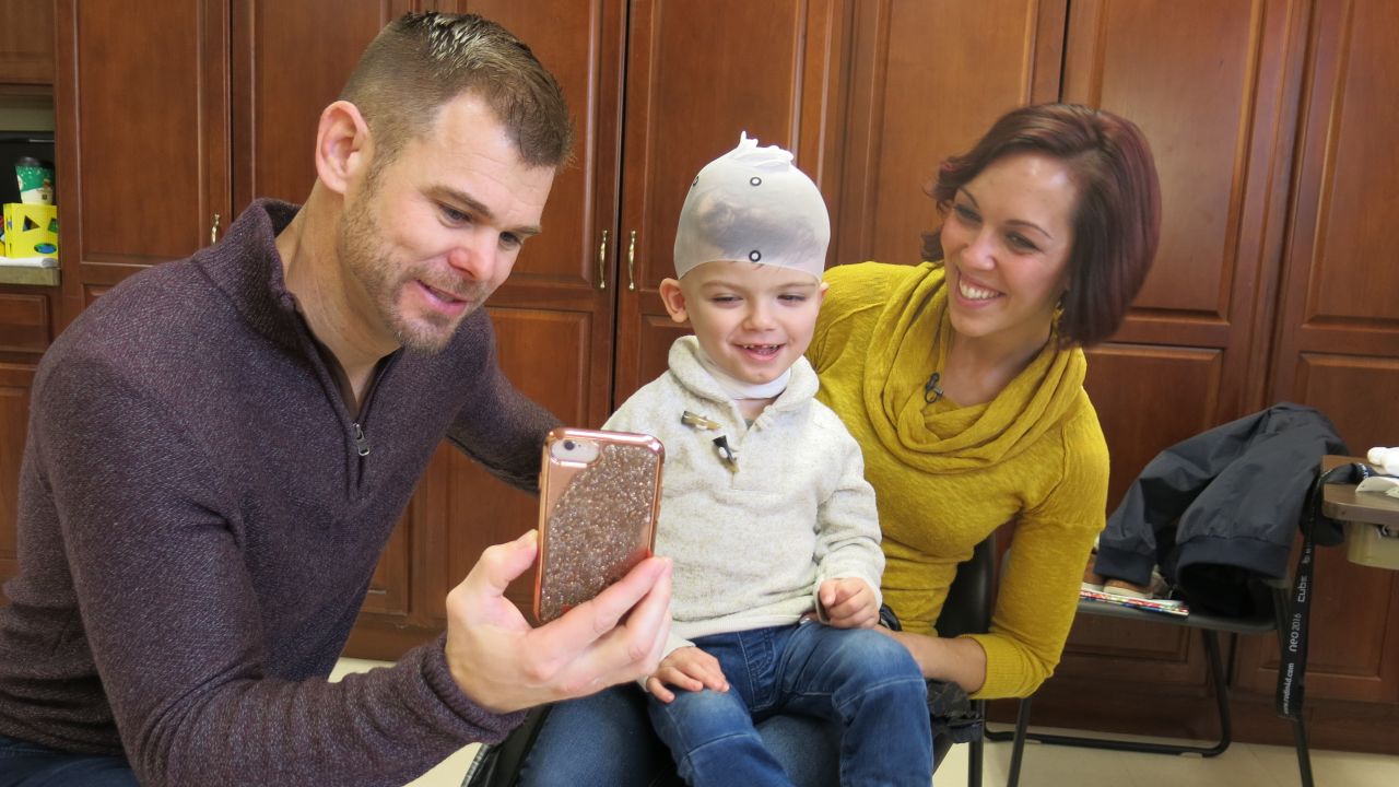 Christian and Nicole McDonald show Jadon photos on a phone while he gets measured for a new protective helmet.