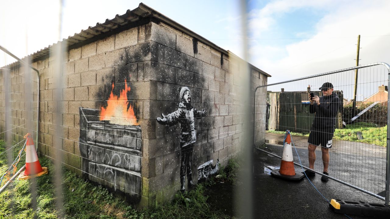 A man takes a photo behind fences in Port Talbot, Wales, that were erected to protect new artwork by the elusive street artist Banksy on Thursday, December 20. <a href="https://www.cnn.com/style/article/banksy-port-talbot-wales-gbr-scli/index.html" target="_blank">The art,</a> which appears to pay homage to the town's industrial past, depicts a child playing in what looks like snow. But viewed from another angle, it appears to be embers and smoke from a dumpster fire.