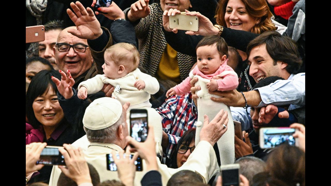 People hold babies in front of Pope Francis as he arrives at a hall in the Vatican on Wednesday, December 19.