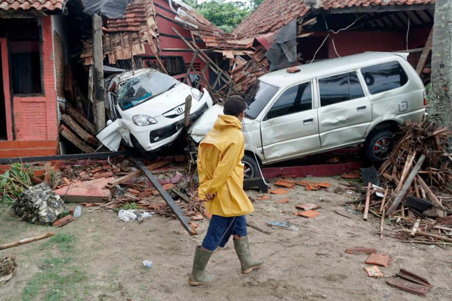 A villager walks past vehicles damaged by a tsunami in Carita, Indonesia.