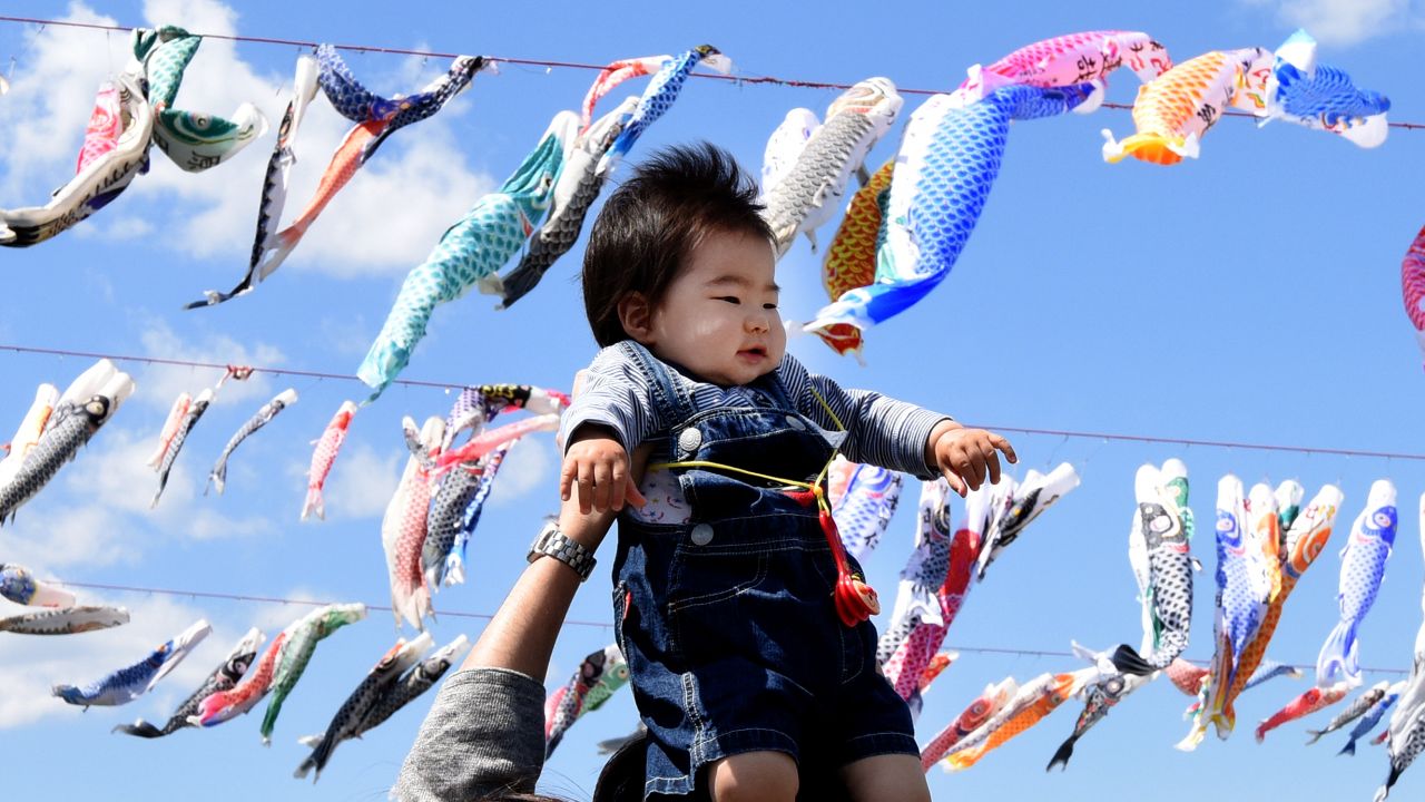 A father holds up his baby under carp streamers fluttering in a riverside park in Sagamihara, suburban Tokyo, on April 29, 2016, ahead of May 5 Children's Day in Japan. 