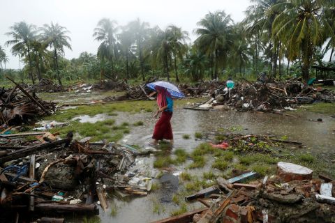 A woman holding an umbrella walks in the rain among debris after the tsunami in Sumur on Wednesday, December 26. 
