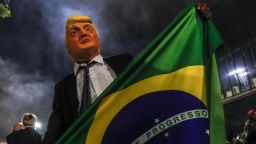 TOPSHOT - A supporter of far-right lawmaker and presidential candidate for the Social Liberal Party (PSL), Jair Bolsonaro, wears a mask of US President Donald Trump as he celebrates after Bolsonaro won Brazil's presidential election, in Sao Paulo, Brazil, on October 28, 2018. - Far-right former army captain Jair Bolsonaro was elected president of Brazil on Sunday, beating leftist opponent Fernando Haddad in a runoff election after a bitter and polarized campaign. Official results gave the controversial president-elect 55.18 percent of the vote with more than 99.7 percent of the ballots counted. (Photo by Miguel SCHINCARIOL / AFP)        