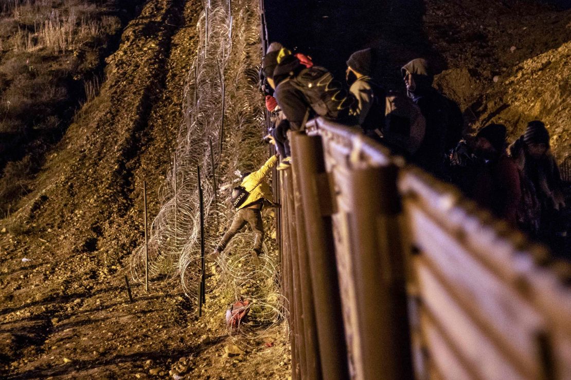 A migrant is lowered toward concertina wire on the US side of the border fence.