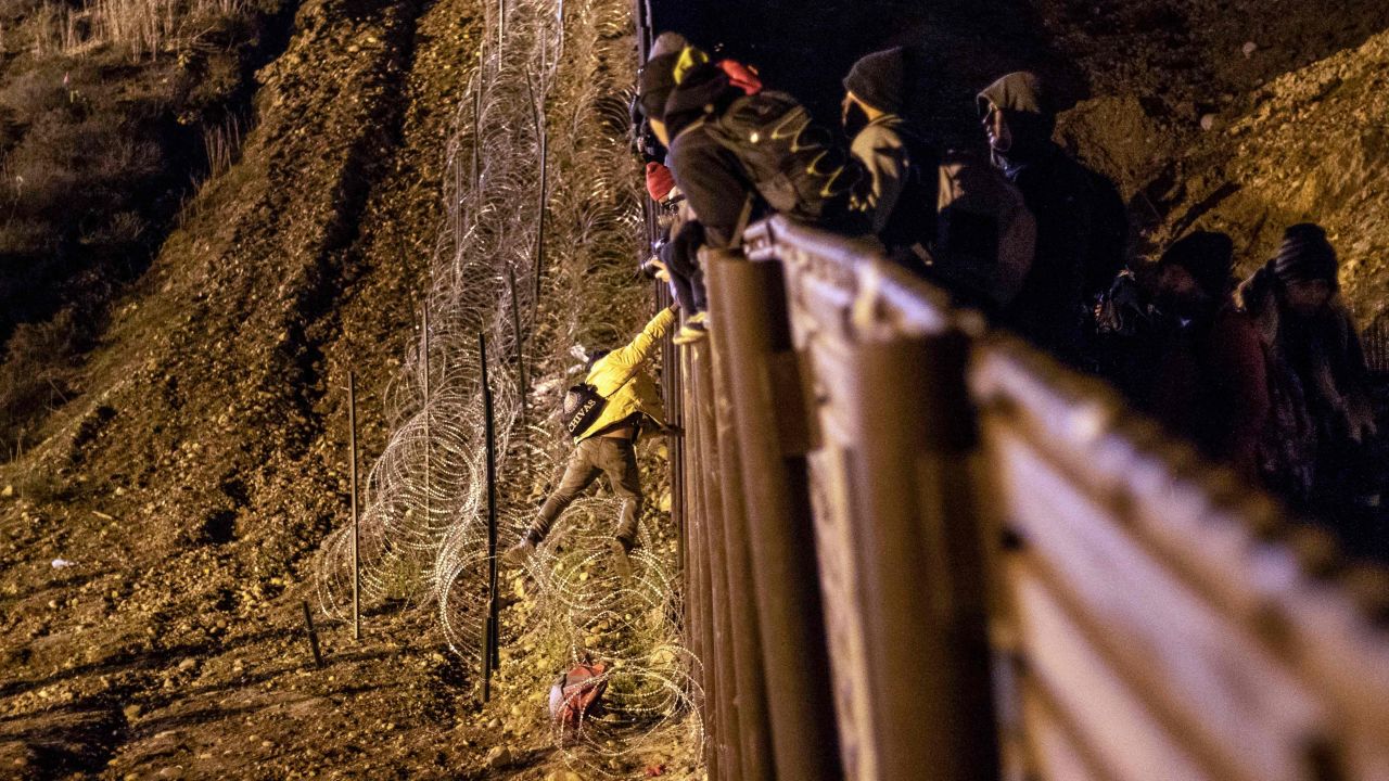 A migrant is lowered toward concertina wire on the US side of the border fence.