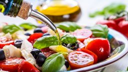 Caprese Italian or Mediterranean salad. Tomato mozzarella basil leaves black olives and olive oil on wooden table.; Shutterstock ID 291753935; Job: -