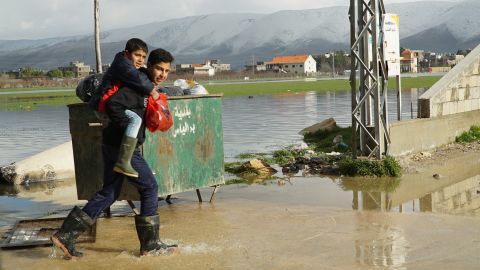 A teenager carries a boy across a flooded street near a Syrian refugee camp.