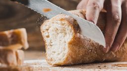 Whole grain bread put on kitchen wood plate with a chef holding gold knife for cut. Fresh bread on table close-up. Fresh bread on the kitchen table The healthy eating and traditional bakery concept; Shutterstock ID 1023191101; Job: -