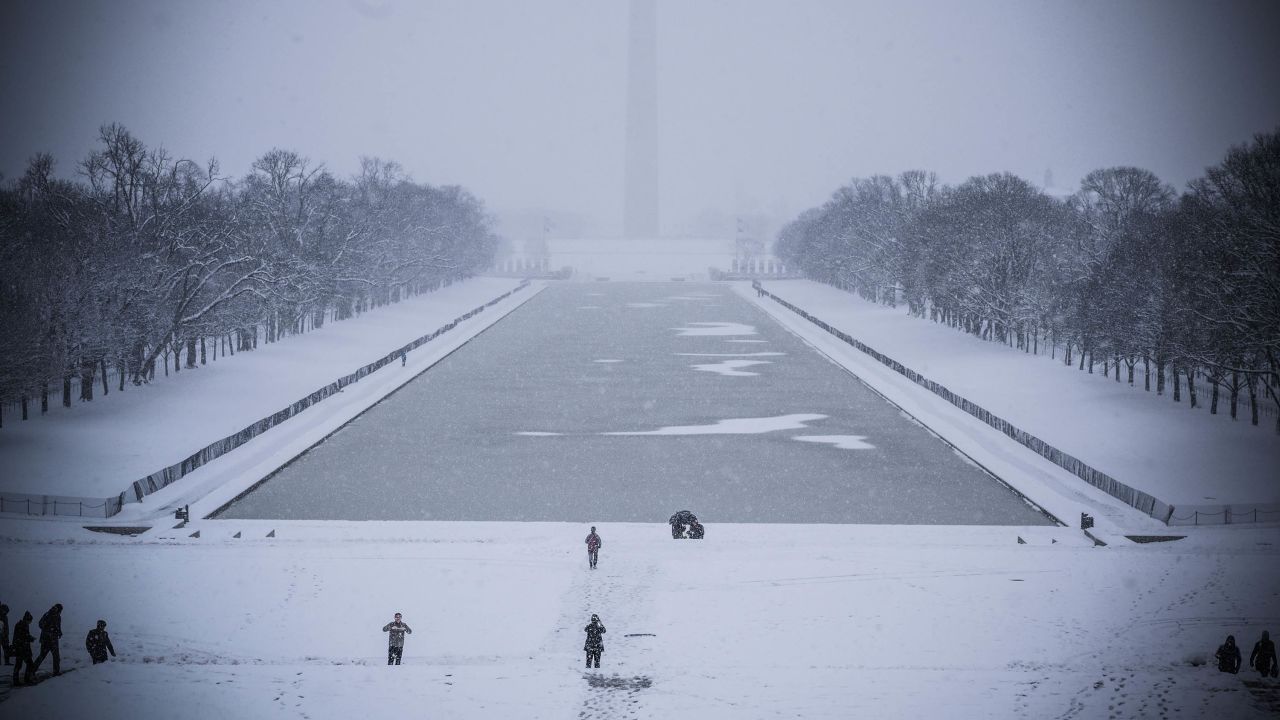 Tourists walk by the Lincoln Memorial reflecting pool as snow covers the ground.