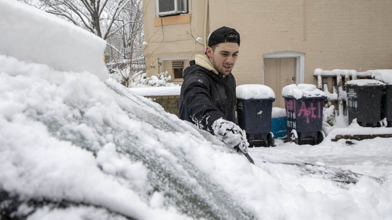 A man brushes snow off his windshield in the Dupont Circle neighborhood of Washington, DC, on January 13, 2019. 
