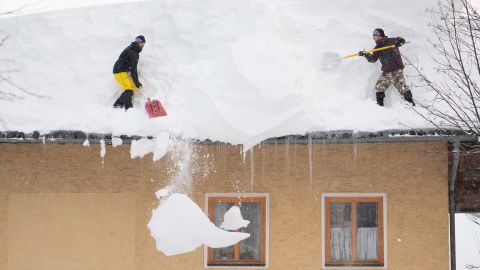 Two men try to remove snow from a roof of a house in Filzmoos, Austria.