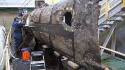 Conservators work to clean away the layer of sand, shells and sea life that collected on the CSS Hunley during the almost 136 years the submarine spent on the sea floor.