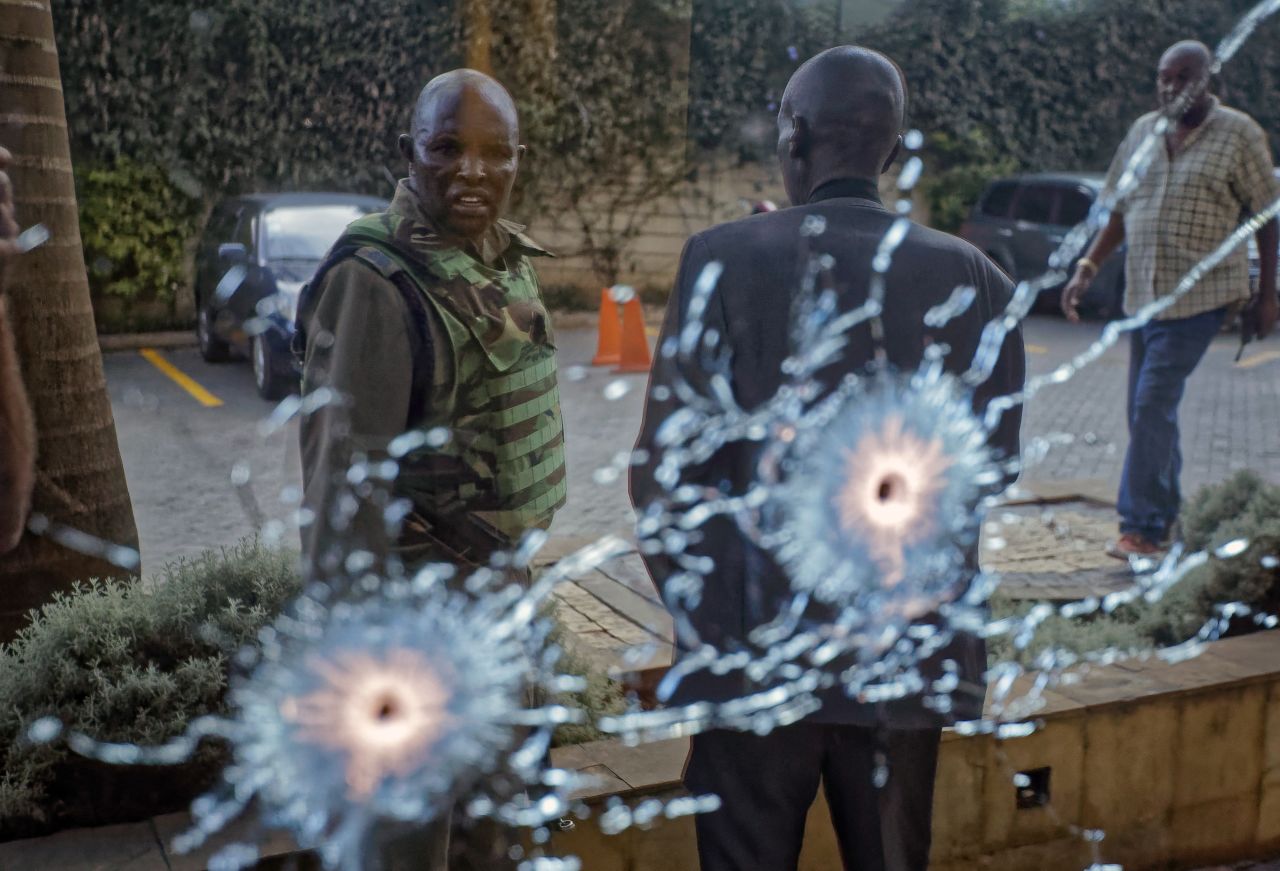 A member of the security forces is seen reflected in a window as he looks at bullet holes.
