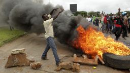 Protestors gather near a burning tire during a demonstration over the hike in fuel prices in Harare, Zimbabwe, Tuesday, Jan. 15, 2019.  A Zimbabwean military helicopter on Tuesday fired tear gas at demonstrators blocking a road and burning tires in the capital on a second day of deadly protests after the government more than doubled the price of fuel in the economically shattered country. (AP Photo/Tsvangirayi Mukwazhi)
