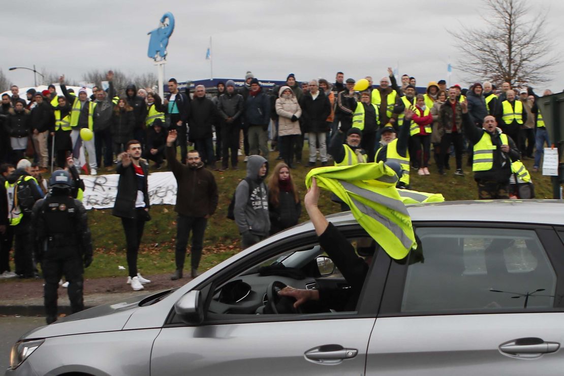A car driver shows his yellow vest to cheer protesters as French President Emmanuel Macron visits Normandy on Tuesday.
