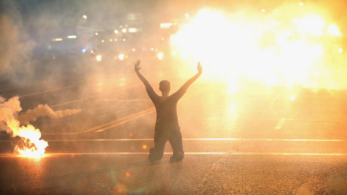 Tear gas drapes a woman kneeling in the street with her hands in the air after 2014 protests against police brutality in Ferguson, Missouri. 