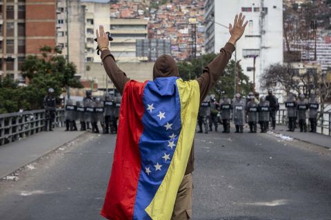 A man wrapped in a Venezuelan flag raises his arms in front of security forces during anti-government protests in Caracas on Wednesday, January 23.