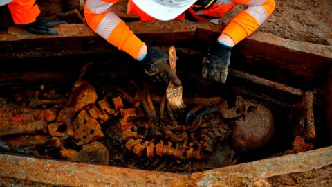 An archeologist uses a brush on a skeleton in an open coffin during the excavation of the cemetery.