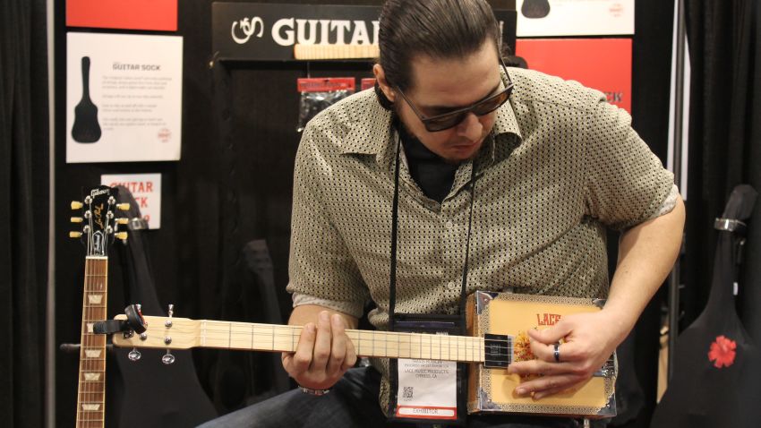 Guitarist Travis Bowlin playing a cigar box guitar made by Lace Music Products at the 2019 NAMM Show.