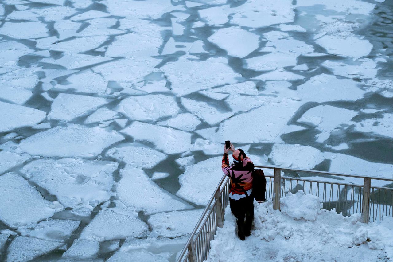 A pedestrian stops to take a photo by the frozen Chicago River.