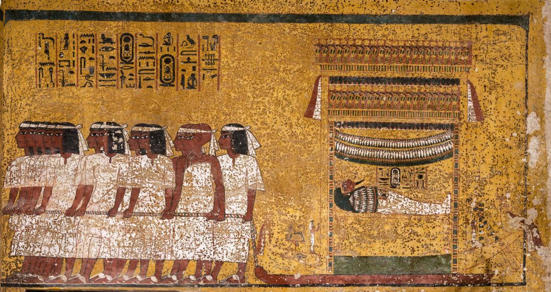 East wall of the tomb's burial chamber. Tutankhamun's mummy is shown, lying in a shrine mounted on a sledge, being drawn by 12 men in five groups. The men wear white mourning bands over their brows. The last pair, distinguished by their shaven heads and different dress, are the two viziers of Upper and Lower Egypt.