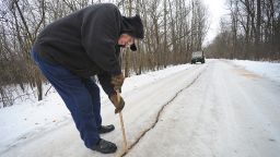In a Saturday, Jan. 11, 2014 photo, Dennis Olsen measures a giant fissure, which he measured to be an inch wide and at least eight to ten inches deep, in his rural driveway in Waupun, Wis., after a weather phenomenon known as an ice quake occured recently. It results from water freezing and expanding in the soil and bedrock. (AP Photo/The Reporter, Aileen Andrews) NO SALES