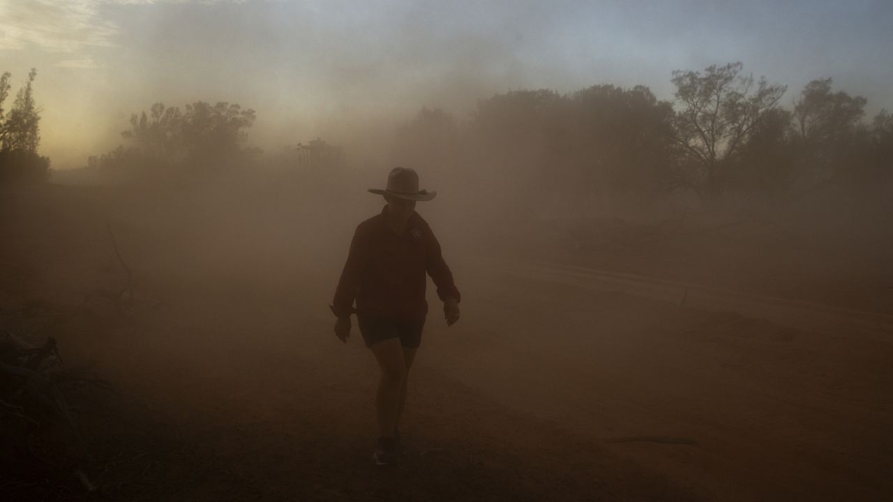 An Australian farmer walks through a cloud of dust on her property on January 16.