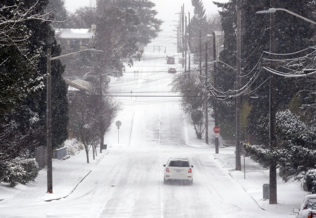 A lone car finds its way along an otherwise deserted street through snow and a cold wind Monday morning in Seattle. 