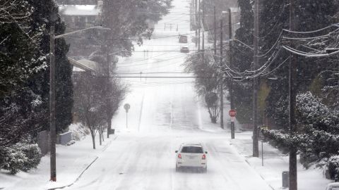 A lone car finds its way along an otherwise deserted street through snow and a cold wind Monday morning in Seattle. 