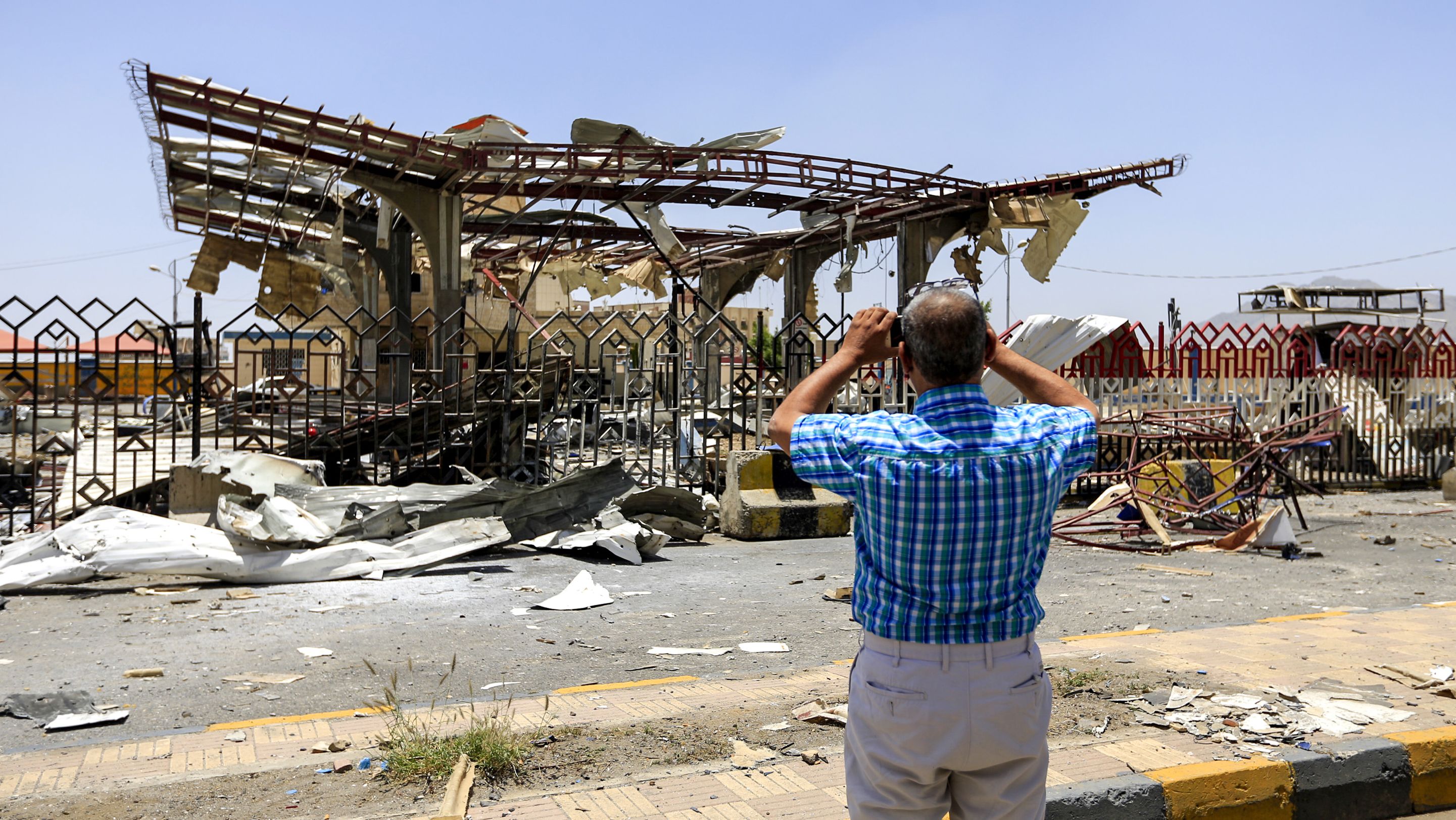 A Yemeni man uses a cell phone to take a picture of a destroyed petrol station that was hit by an airstrike in the capital Sanaa on May 27, 2018.