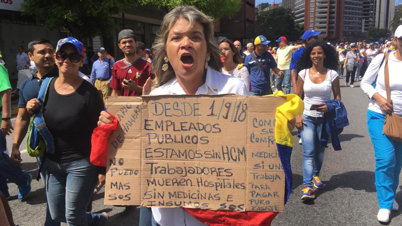 An anti-Maduro protester carries a cardboard poster which reads: "Since 1/9/18 public servants have gone without health insurance. Workers are dying. Hospitals don't have medicines or supplies. SOS"