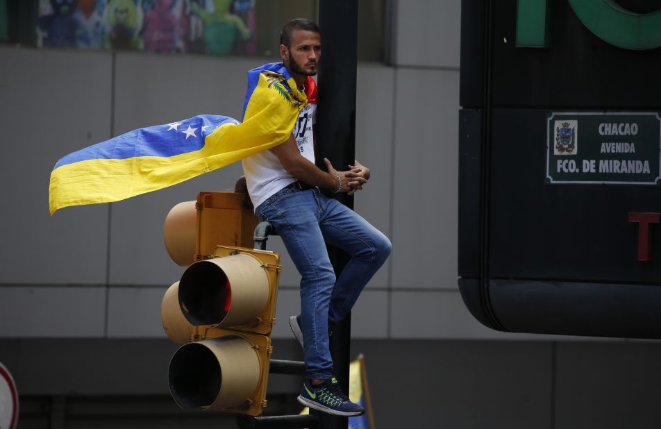 A man wearing a Venezuelan flag sits on a traffic light during the demonstration in Caracas on February 12.