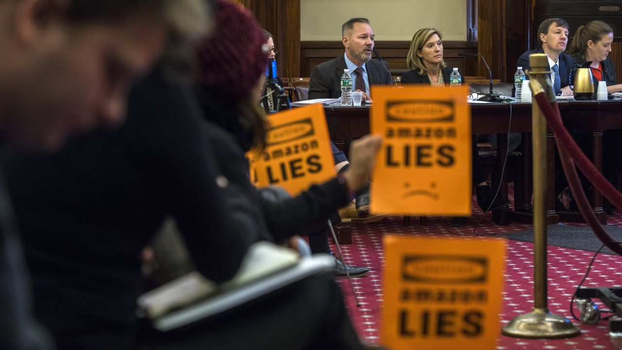 Protesters hold up signs as executives from Amazon testify at a City Council hearing.