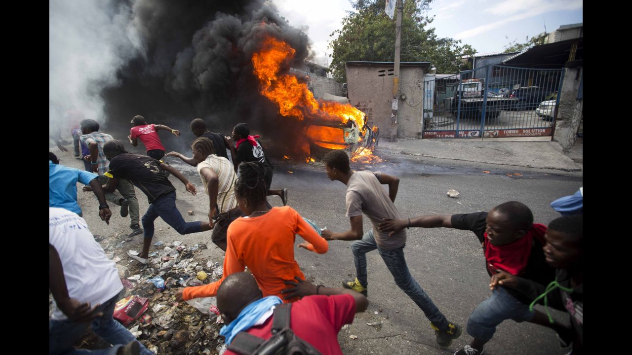 Protesters demanding the resignation of Haitian President Jovenel Moise run away from police shooting in their direction as a car burns nearby in Port-au-Prince, Haiti, on Tuesday, February 12.