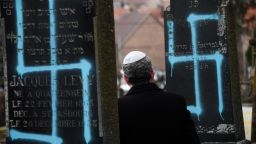 A man walks by graves vandalised with swastikas at the Jewish cemetery in Quatzenheim, on February 19, 2019, on the day of a nationwide marches against a rise in anti-Semitic attacks. - Around 80 graves have been vandalised at the Jewish cemetery in the village of Quatzenheim, close to the border with Germany in the Alsace region, which were discovered early February 19, 2019, according to a statement from the regional security office. 