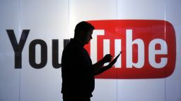 A man is seen as a silhouette as he checks a mobile device whilst standing against an illuminated wall bearing YouTube Inc.'s logo in this arranged photograph in London, U.K., on Tuesday, Jan. 5, 2016. YouTube Inc. provides consumer media and entertainment through its website. Photographer: Chris Ratcliffe/Bloomberg via Getty Images