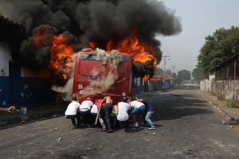 Demonstrators push a bus that was set on fire during clashes with the Venezuelan National Guard in Urena, Venezuela, on February 23.