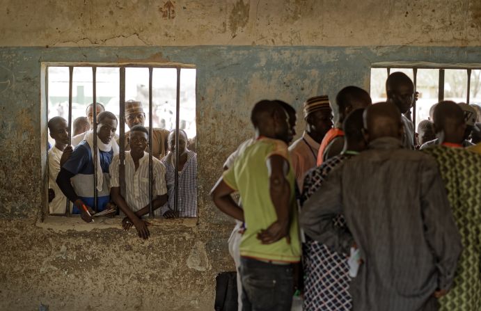People peer through a window as party agents huddle together to watch votes being counted inside a polling station in Kano, Nigeria.