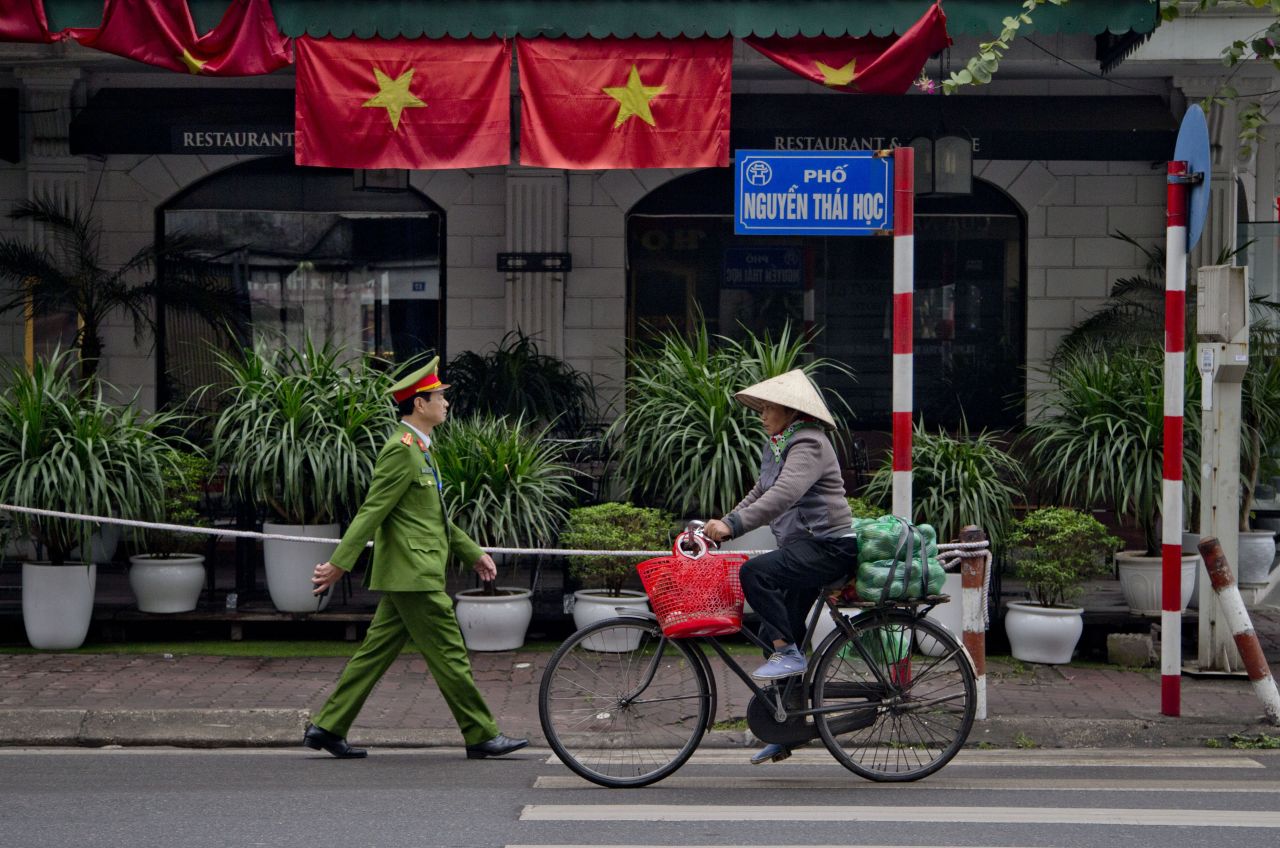 A woman rides a bicycle as a police officer walks past Vietnamese flags in Hanoi on February 27.