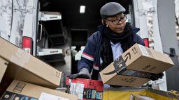 A letter carrier holds Amazon.com Inc. packages while preparing a  vehicle for deliveries at the United States Postal Service.