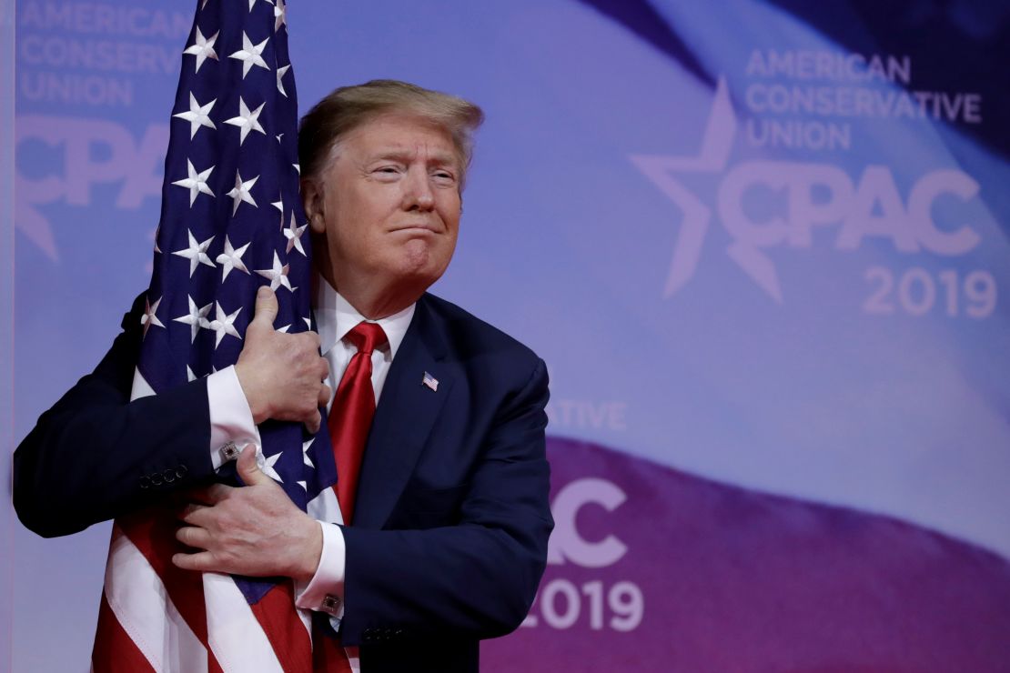 President Donald Trump hugs American flag at the CPAC annual meeting, March 2, 2019.