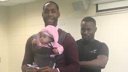 Wayne Hayer helps fasten his daughter Assata in a harness worn by his professor, Nathan Alexander. The professor offered to carry the baby during class so Hayer could take notes.
