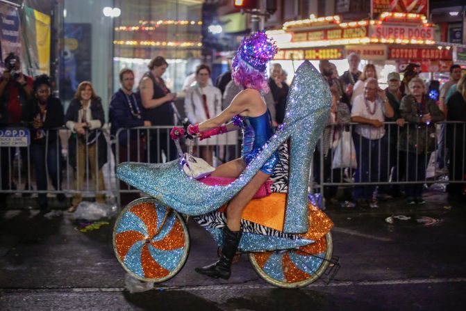 A woman rides in the parade on a bicycle decorated like a high-heel shoe.