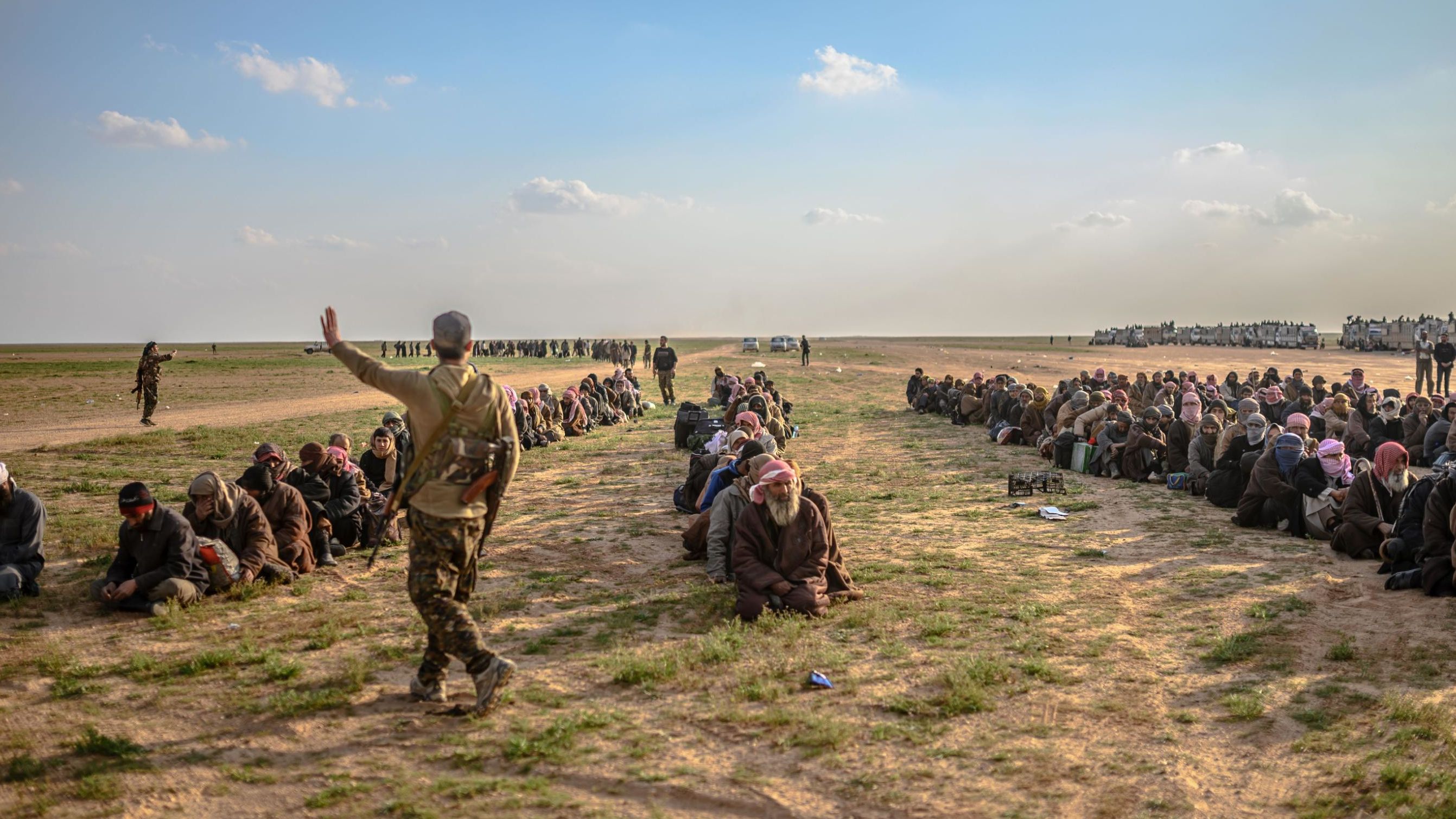 Men suspected of being ISIS fighters wait to be searched by SDF members after leaving Baghouz.