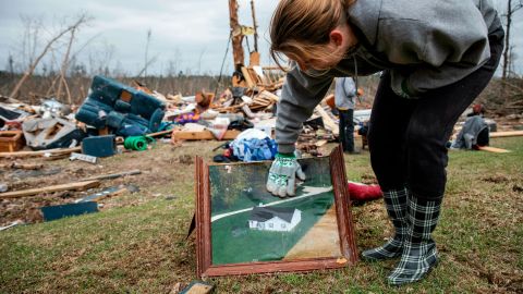 Debris from a friend's home stands in the background as Ashley Griggs wipes away dirt from a photo found in the rubble of what it used to look like before it was destroyed by a tornado.