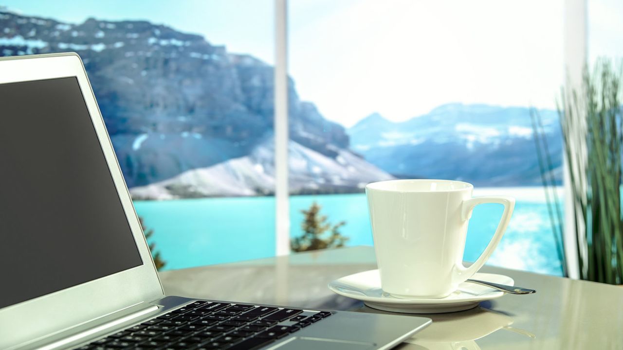 A laptop and a cup of tea or coffee, with view of mountain or lake beyond