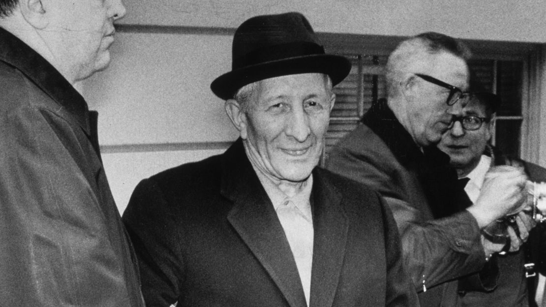 Mob boss Carlo Gambino smiles while standing in handcuffs after being arrested by the FBI. 
