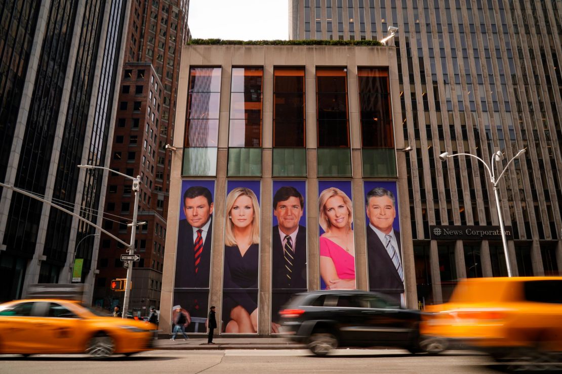 Traffic on Sixth Avenue passes by advertisements featuring Fox News personalities, including Bret Baier, Martha MacCallum, Tucker Carlson, Laura Ingraham, and Sean Hannity, adorn the front of the News Corporation building.