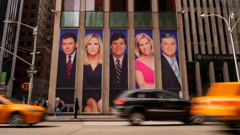Traffic on Sixth Avenue passes by advertisements featuring Fox News personalities, including Bret Baier, Martha MacCallum, Tucker Carlson, Laura Ingraham, and Sean Hannity, adorn the front of the News Corporation building.