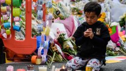 A child sits among flowers and candles left in tribute to the victims after a vigil in Christchurch on March 18, 2019, three days after a shooting incident at two mosques.